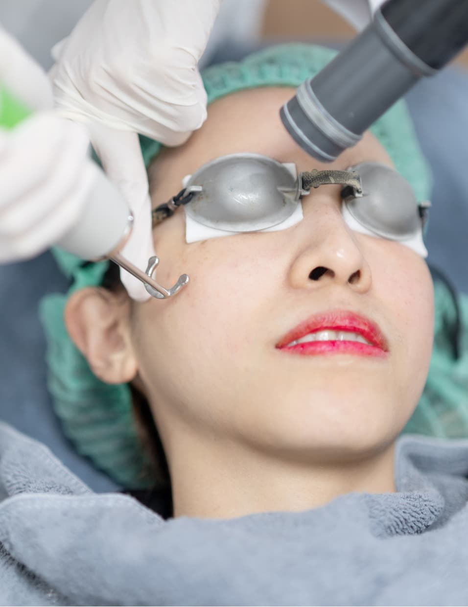 a close-up shot of a woman wearing a head cover with her eyes covered in plastic goggles undergoing a pico laser treatment